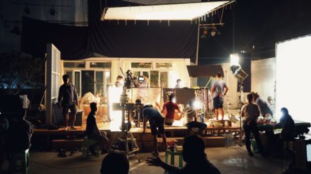 Blurry image of making movie video in big production studio and film crew team shooting or recording by professional digital camera and lighting set equipment.