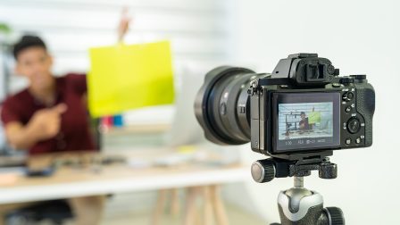 Young asian male online merchant blogger recording live vlog video with colorful shopping bag preparing for sale and review goods at home. Online influcencer on social media concept. Focus on camera